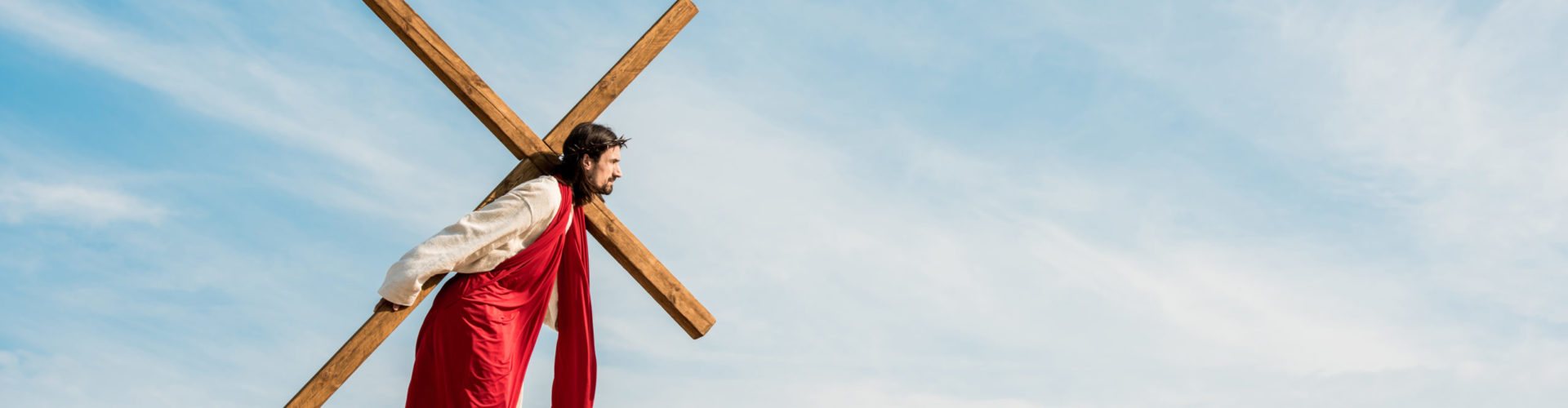 Panoramic shot of bearded man walking with wooden cross
