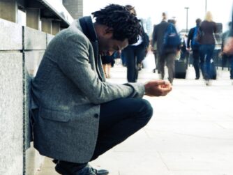 Commuters rush past a homeless character on their way to the office.