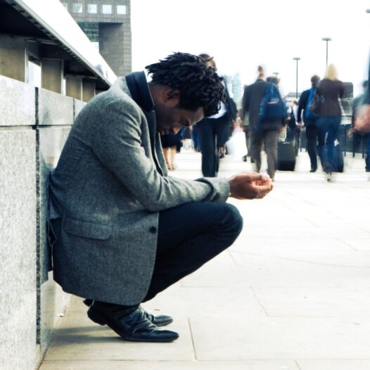 Commuters rush past a homeless character on their way to the office.